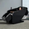Panasonic MAN2 Massage Chair Model Lifestyle Woman relaxing in a reclined black Panasonic MAN2 5D A.I. massage chair next to a city-view window.